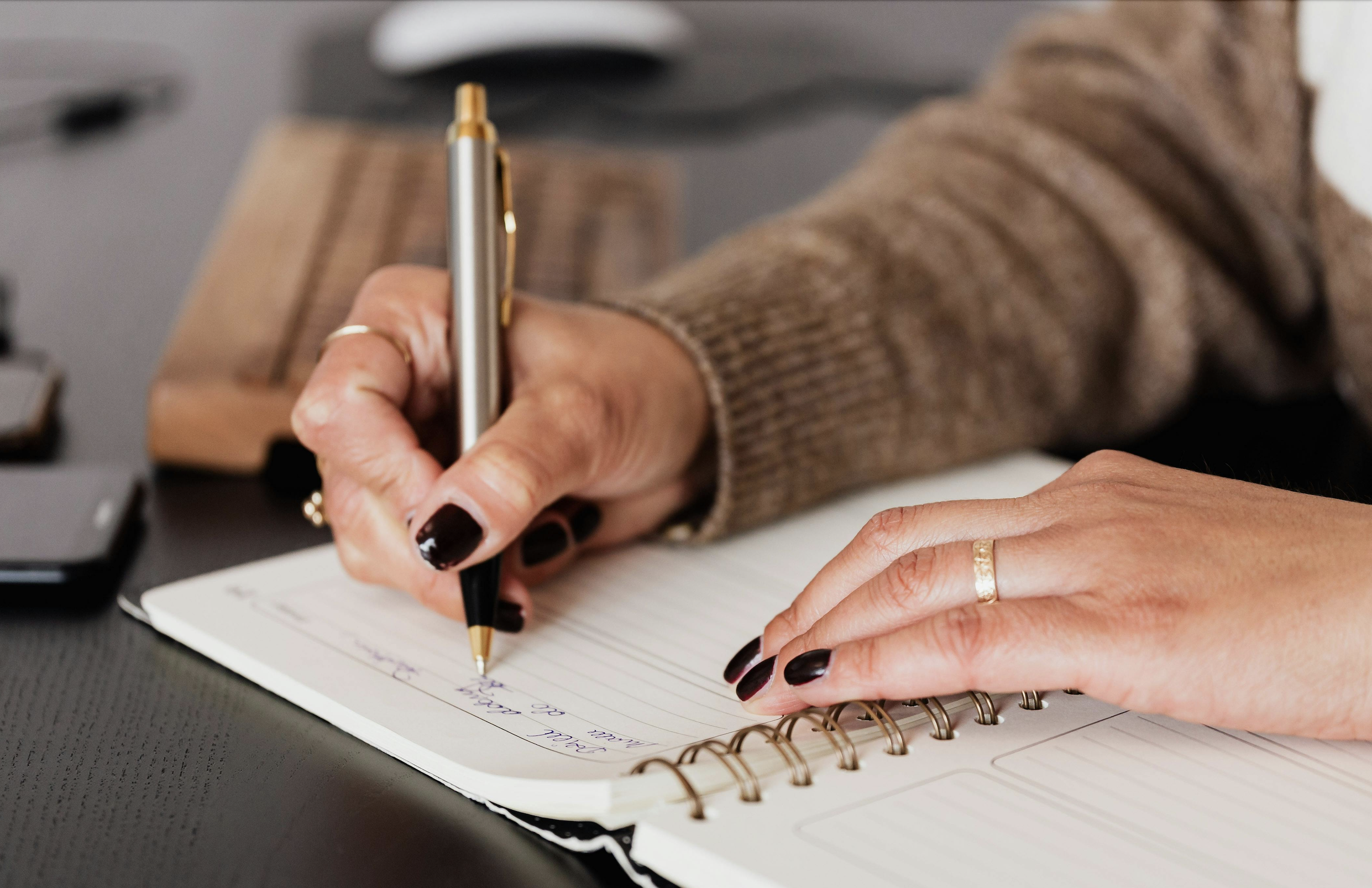 Woman's hands writing in a notebook with a pen.